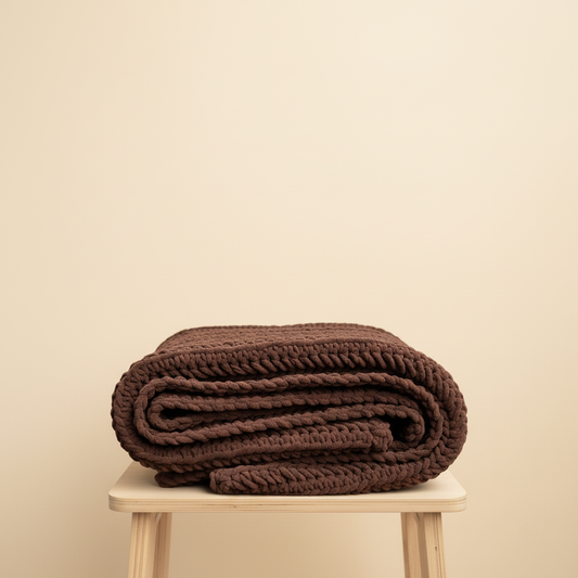 Folded brown blanket on a wooden stool against a beige background